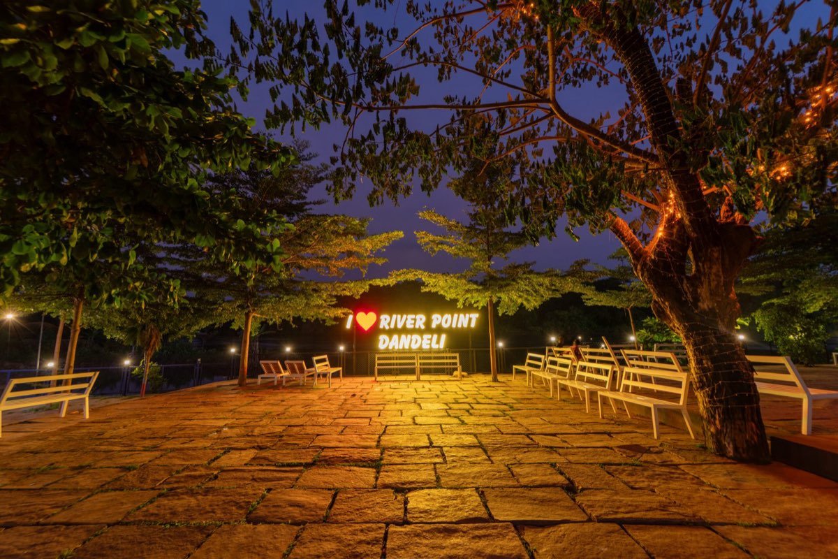 Lit riverside seating with the River Point Dandeli sign at night